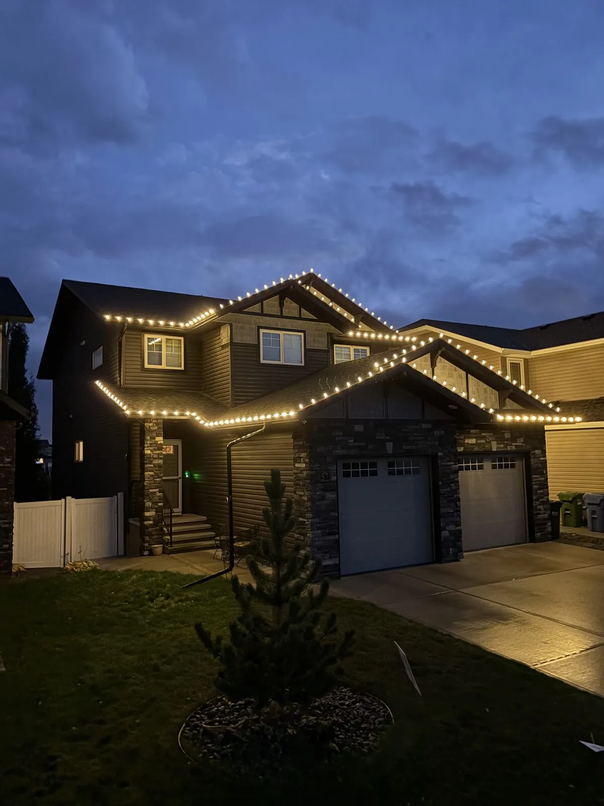 Two-storey home with warm white C9 lights along every roofline and gable, photographed at dusk