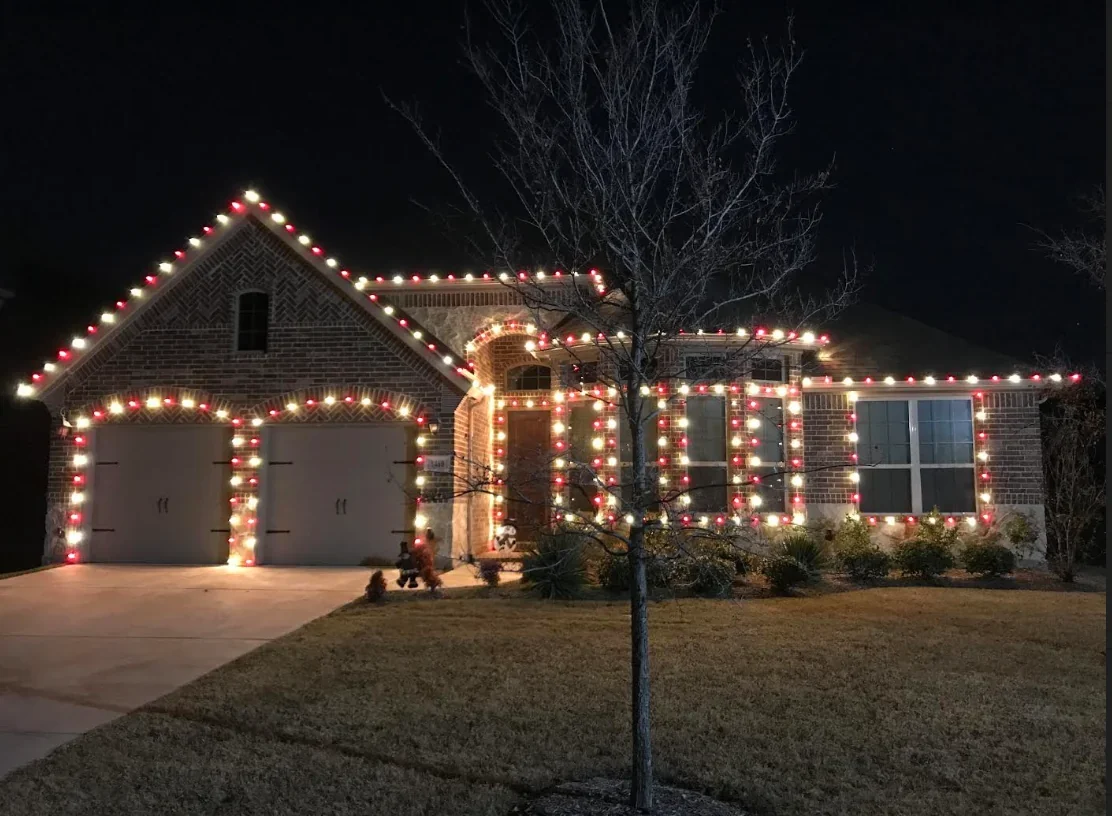 Brick home at night outlined in classic red and white C9 lights along the rooflines, garage doors and windows